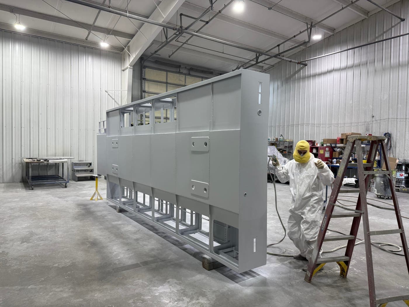 Worker spray painting a large industrial enclosure in the Werco paint booth