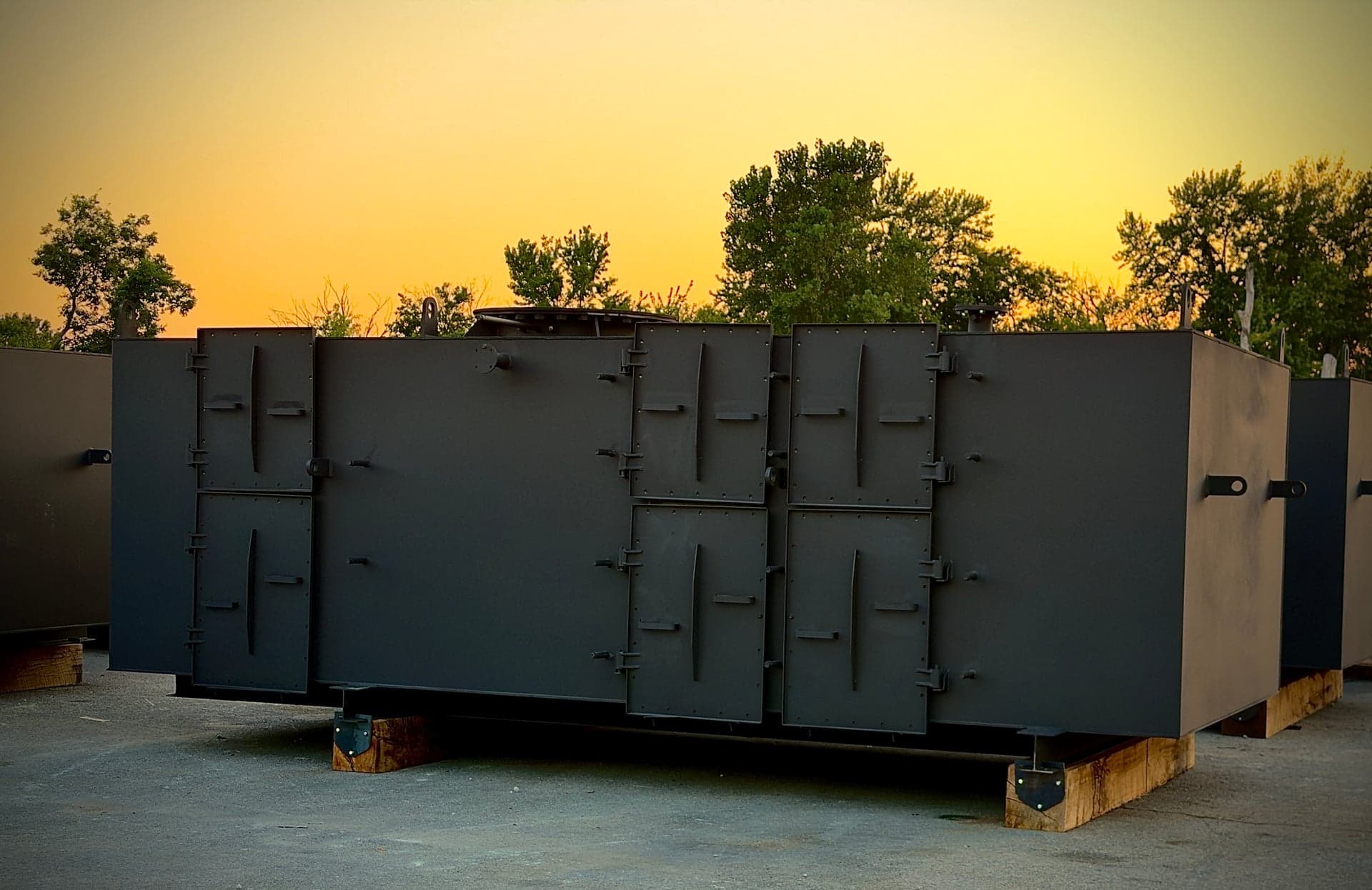 Painted industrial enclosure assemblies with access doors and lifting points at sunset